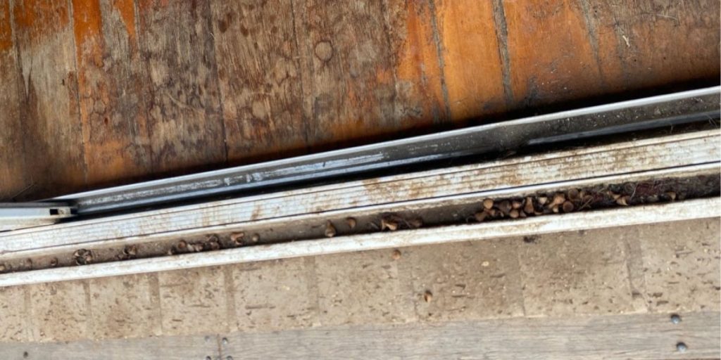 Sliding door track clogged with dirt and debris before cleaning